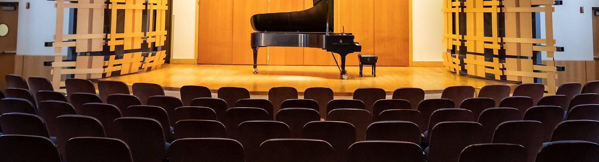 An unattended piano on a stage in an empty auditorium. 