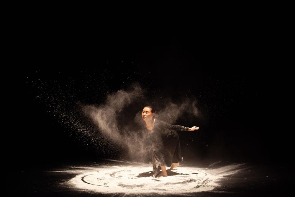 A dancer performs on stage, swirling in sand, creating a unique visual effect.
