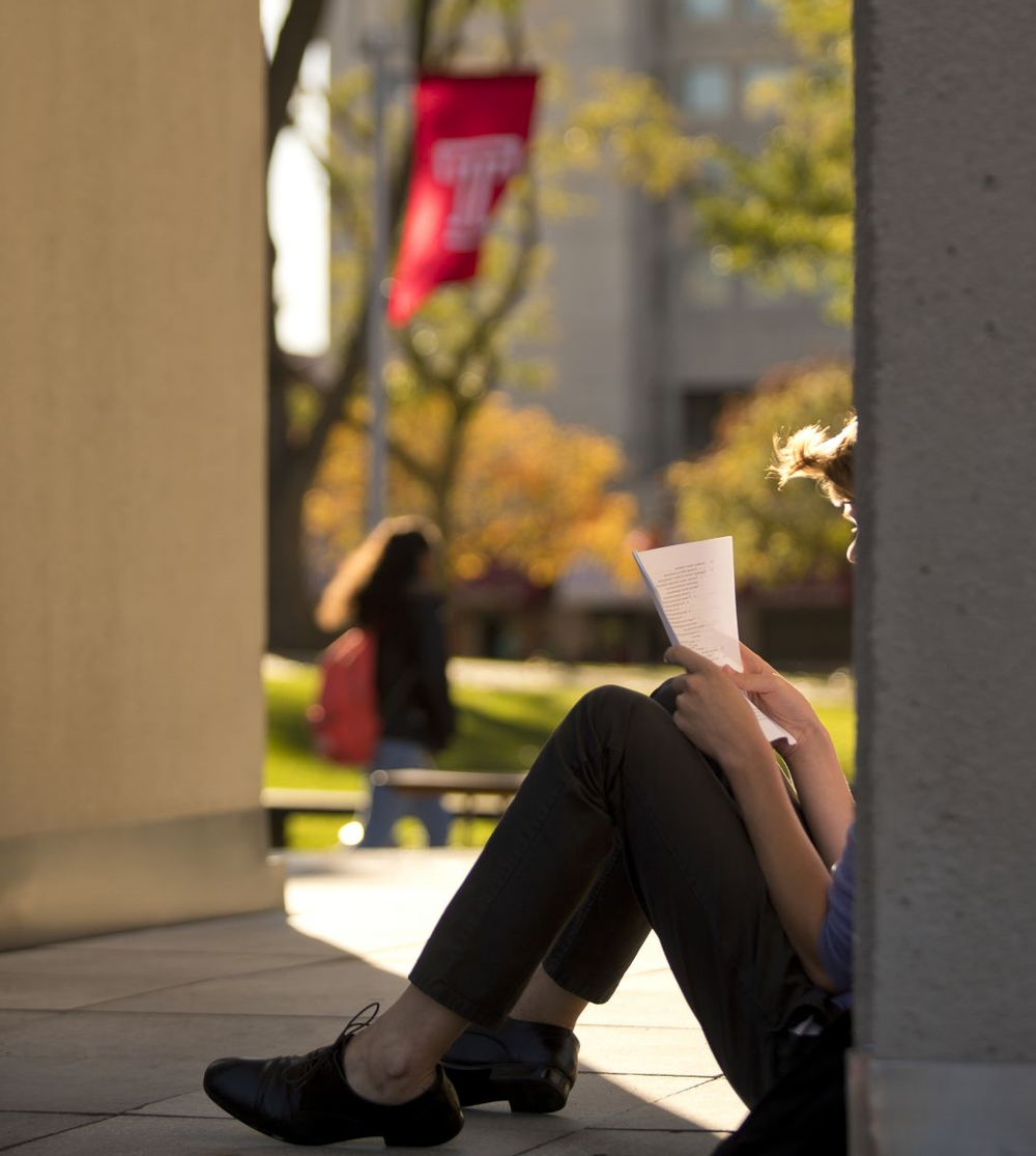 在一个阳光明媚的下午，一个学生坐在阴凉处看一袋报纸